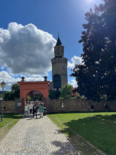 Besucher:innen gehen durch das Tor. Im Hintergrund der Hexenturm